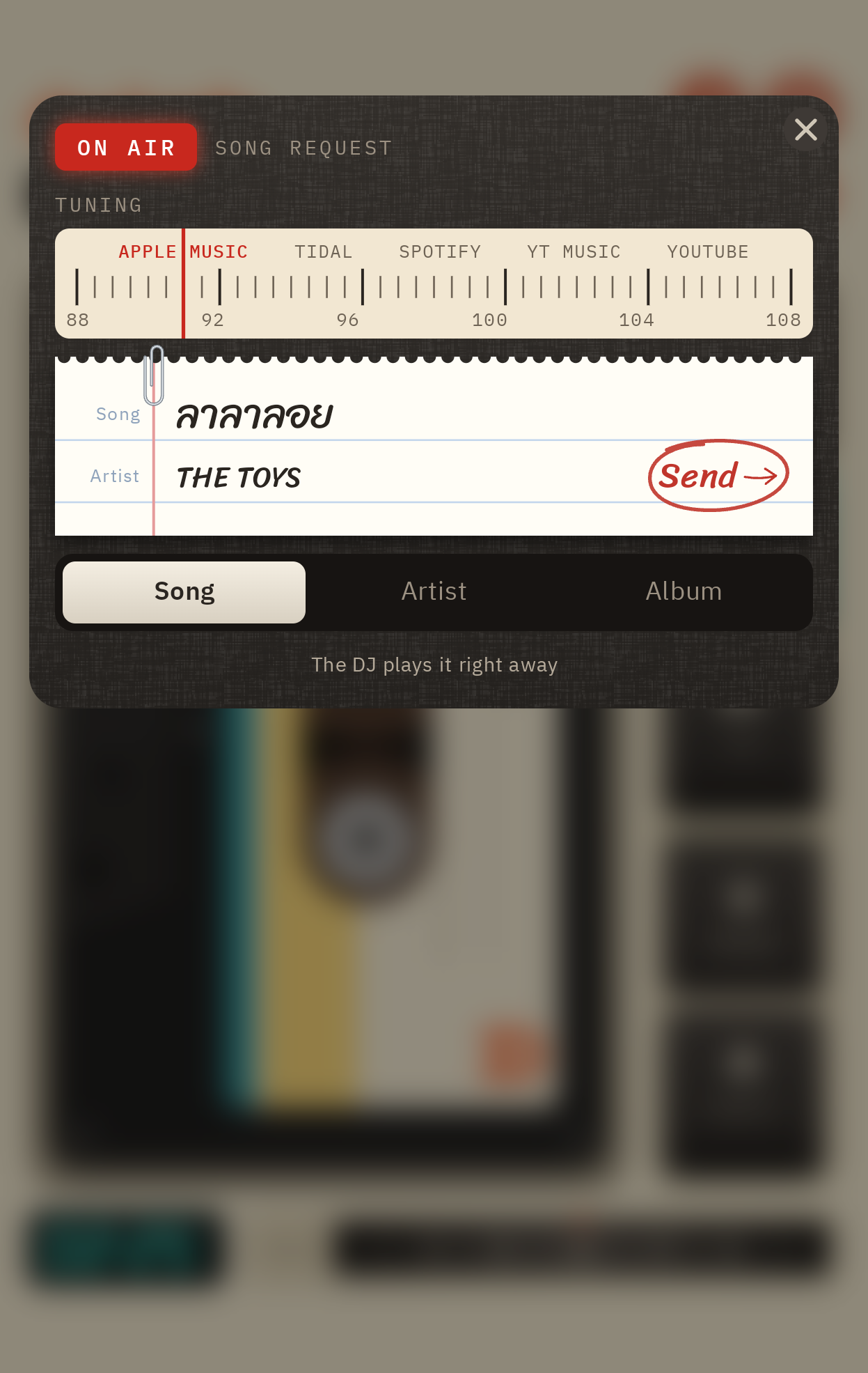 แผงขอเพลงบนจอนอก: แถบจูนสถานีอยู่ที่ Apple Music กระดาษโน้ตเขียนด้วยลายมือว่า ลาลาลอย ของ THE TOYS มุมขวาล่างวงคำว่า Send ด้วยปากกาแดง เครื่องเล่นเทปด้านหลังเบลอ